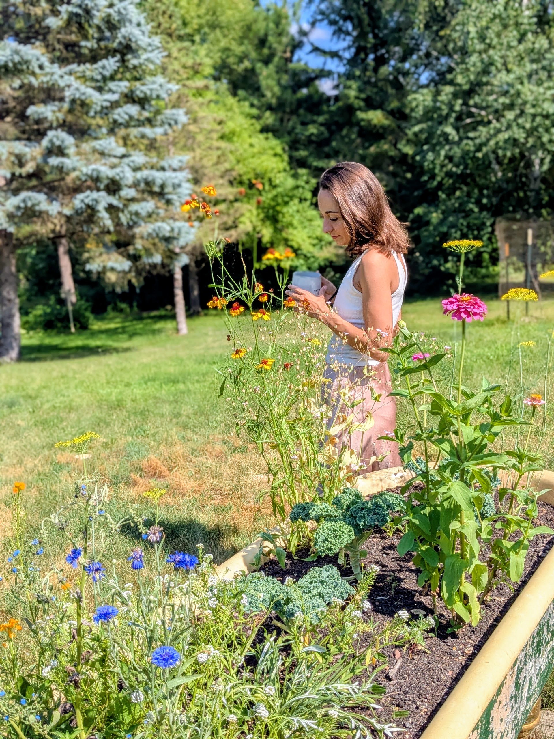 Sanja standing among flowers in a sunny garden.